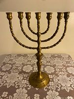 Front view of the vintage brass menorah showing seven branches and circular base with decorative elements on a lace patterned cloth.