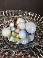 Top view of collection of vintage opaque glass marbles with various colored swirls in a clear cut glass dish.