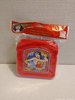 Front view of bright red sandwich container with a colorful Wonder Woman comic style image, sealed in original packaging with header showing branding and product title.