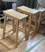 Two solid wood counter stools placed on a wooden floor, showing front and side views.