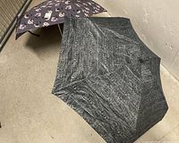 Photo showing two umbrellas open on the floor, one black textured swirl pattern, one floral pattern.