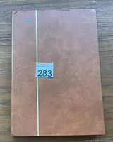 Closed brown stamp album with vertical gold stripe on cover and lot sticker 283.
