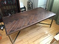 Angled side view of the rectangular coffee table showing the wood top's herringbone pattern and bronze finish metal legs.