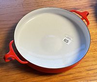 Top view of the red enameled paella pan showing off-white interior and two red handles on opposite sides on wooden surface