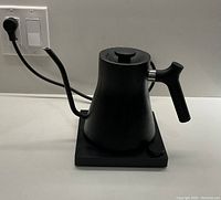 Front angled view of the black Fellow Stagg EKG electric kettle on its base with power cord and control knob visible.