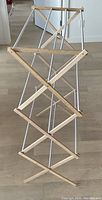 Collapsible clothes drying rack folded compactly showing wooden frame and metal support rods.