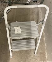 Close-up photo showing top view of the white Mastercraft 2 step ladder, highlighting the ribbed non-slip steps and handle.