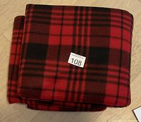 Folded red and black plaid electric heated car blanket with lot number sticker.