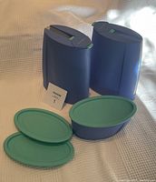 Two large blue Tupperware containers with closed green oval lids and one smaller blue container with two green oval lids placed in front.