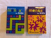 Two boxed sets of Mensa cards for kids, one mind mazes and one word puzzles, placed on a white textured surface