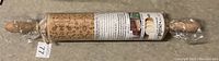 Rolling pin wrapped in plastic, showing engraved pattern and label.