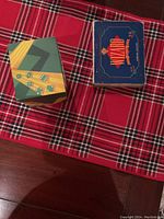 Two card game boxes: one with dice pattern (Telestrations After Dark), one blue box (Wizard) on red plaid tablecloth.