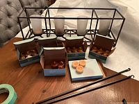 Photo showing bronze plated hanging candle holder with four frosted glass candle cups and multiple boxes of candles in various colors in front.