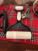 Close-up of black and white handheld strainer and roller pan scraper on red plaid cloth