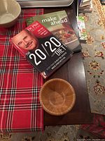 Photo of two books and a small bamboo bowl on a wooden surface with red plaid cloth
