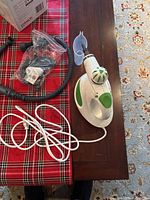 Polti handheld steam sanitizer on table with power cord, flexible hose, and multiple black nozzle attachments in plastic bag, plus measuring cup.