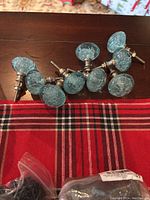 Nine blue glass drawer pulls laid out on a table with a red plaid cloth beneath them, showing textured glass design and metal screws.