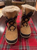 Front view of Sorel winter boots showing the lace-up front, brown suede upper, black rubber lower, and plush faux fur lining at the top.