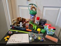 Clear view of assorted toys arranged on a flat surface including plush bears, figurines, rubber balls, colorful boxes, and a safari tin bucket.