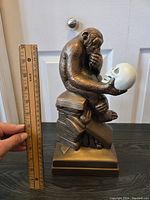 Front view of sculpture showing chimpanzee holding skull and stacked books, ruler for scale