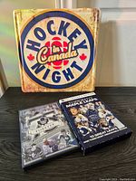 Photo showing the Hockey Night in Canada metal wall sign and two Toronto Maple Leafs DVDs placed on a dark wooden surface.