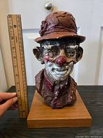 Front view of signed clown bust with ruler showing approx. 10 inches height. Shows facial details and hat with flower.