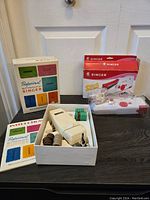 Photo of the Singer Professional Buttonholer set in its original box with instruction booklet and work accessories on display.