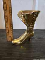 Side view of brass lady's boot figurine with ruler showing height approximately 7 inches, highlighting detailed lacing and button decoration.
