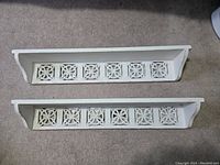 Two white wooden wall shelves laid on carpet with decorative mirrored square details visible.