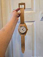Full view of wooden wall clock resembling a wristwatch, held by hand to show size and design.