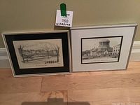 Two framed artworks on the floor: left artwork is a pencil sketch titled 'The Metal Bridge, Dublin' by Judges with black mat and silver frame; right artwork is a print titled 'The Four Courts, Dublin' by Fergus A Ryan with white mat and silver frame.