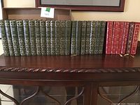 Photo showing full collection of green hardcover Charles Dickens Complete Works volumes along with red and brown leather-bound books on a wooden shelf.