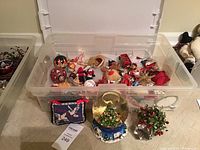 Clear plastic bin containing assorted small Christmas ornaments including Santa Claus, reindeer, and tree decorations