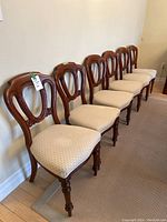 Six medium wood dining chairs with carved backs and beige basket weave seats arranged in a row