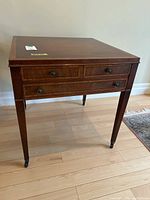 Front view of the square wood side table showing three drawers with round knobs and tapered legs on castors.