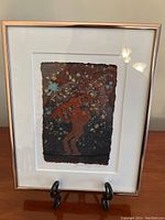 Front view of framed art showing petroglyph figure on black background in rose gold tone frame with stand.