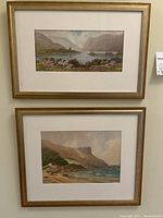 Full view of both framed landscape prints stacked vertically on wall showing gold-toned brushed metal frames and white mats.