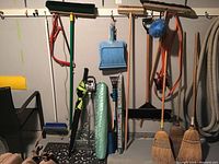 Full view of the wall with hanging brooms, dustpans, bow saw, tarp roll, and hooks