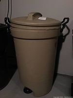 Front view of the large beige Rubbermaid garbage can with lid and black side handles