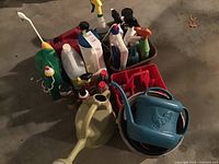 Photo showing various cleaning bottles, sprays, and two watering cans in plastic containers on garage floor