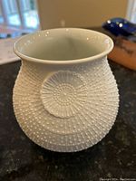 Front view of white ceramic Kaiser vase showing dotted texture and floral embossed medallion.