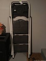 Folded metal 3-step ladder showing white frame and black steps, plastic top tray visible.