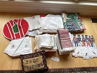 Full view of assorted placemats, napkins, embroidered white linens, quilted holiday-themed cloths, and True Friends pillow on a wooden floor.