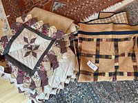Folded view of two matching quilts showing floral and geometric patterns with scalloped edges next to folded beige quilt with plaid accents