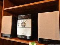 Front view of Sony micro hi-fi stereo main unit with 2 separate speakers on shelf.