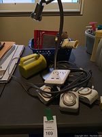 Full view of the silver task lamp, yellow flashlight, basket with tape dispenser, felt pads, and multiple lamp timers on table.