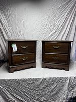 Two dark hardwood side tables with two drawers each, positioned side by side, visible wear and missing handle on one drawer.
