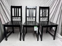 Front view of three black wooden dining chairs, highlighting square seats and vertical slat backrests