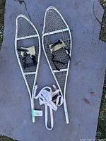 Pair of aluminum snowshoes laid on a cloth surface, shows frame, mesh decking, bindings, and extra laces.
