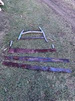 Five antique metal crosscut saws laid on grass, including three long saws and one smaller bow saw frame, all rusty.